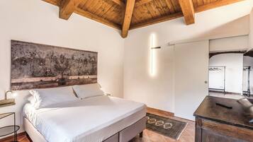 A bedroom with a bed, a large painting, a bedside table, a desk, and a mirror.
