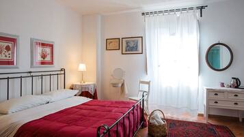 A bedroom with a bed, a bedside table with a lamp, a chair, a dresser, a mirror, and a window with curtains.