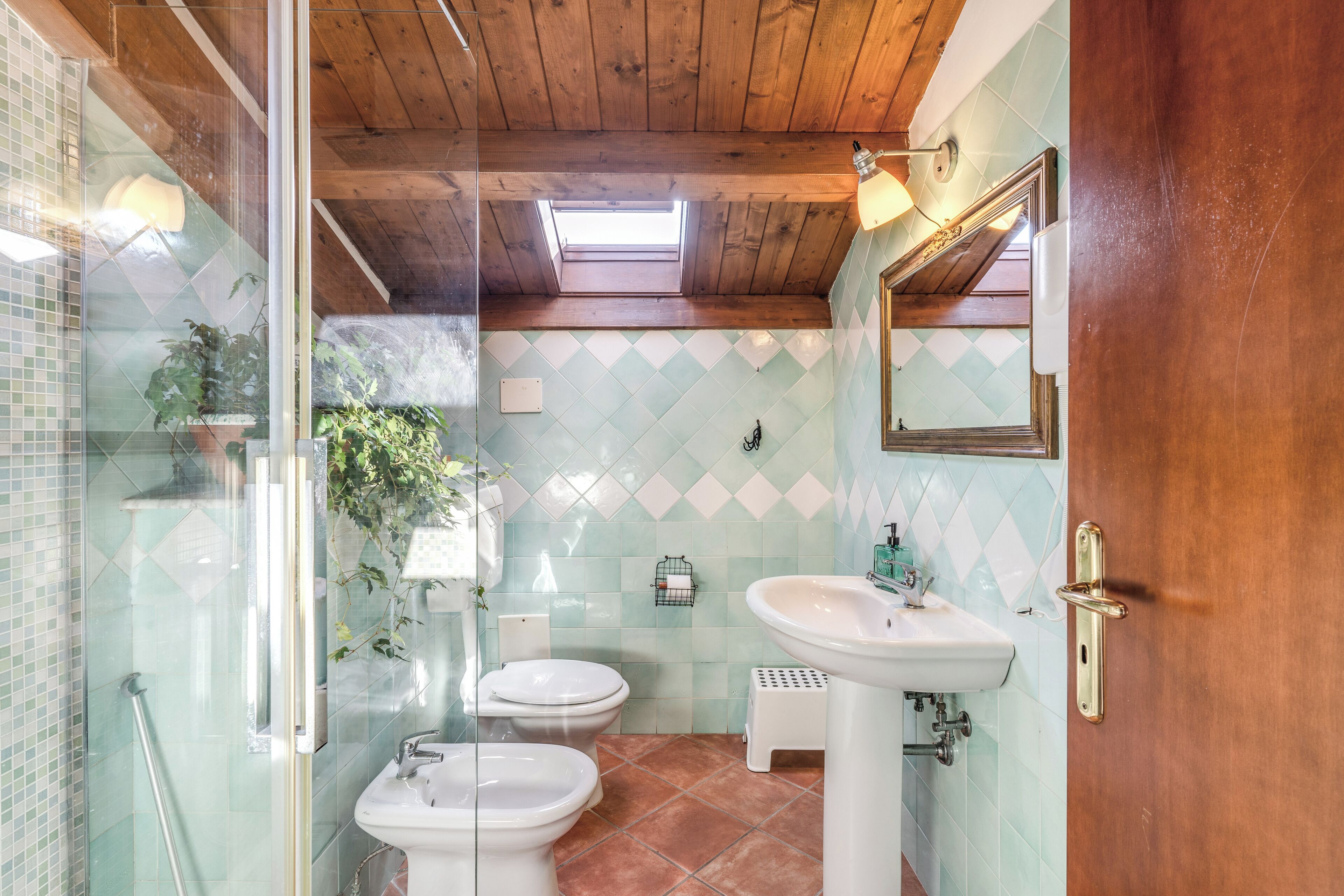 Un baño con cabina de ducha de vidrio, dos inodoros, un lavabo y un espejo.