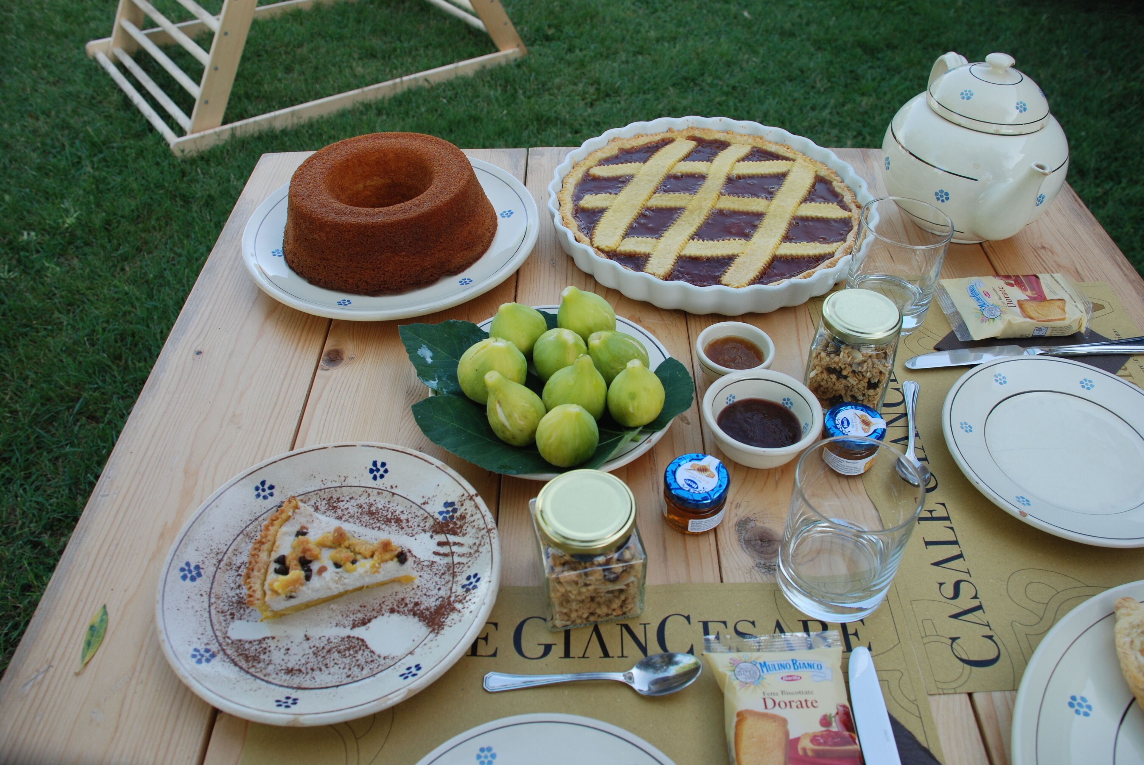 Une table de pique-nique avec un gâteau, une tarte, un service à thé et divers condiments.