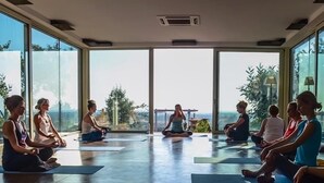 A yoga class in a spacious room with large windows and a view of the outdoors.