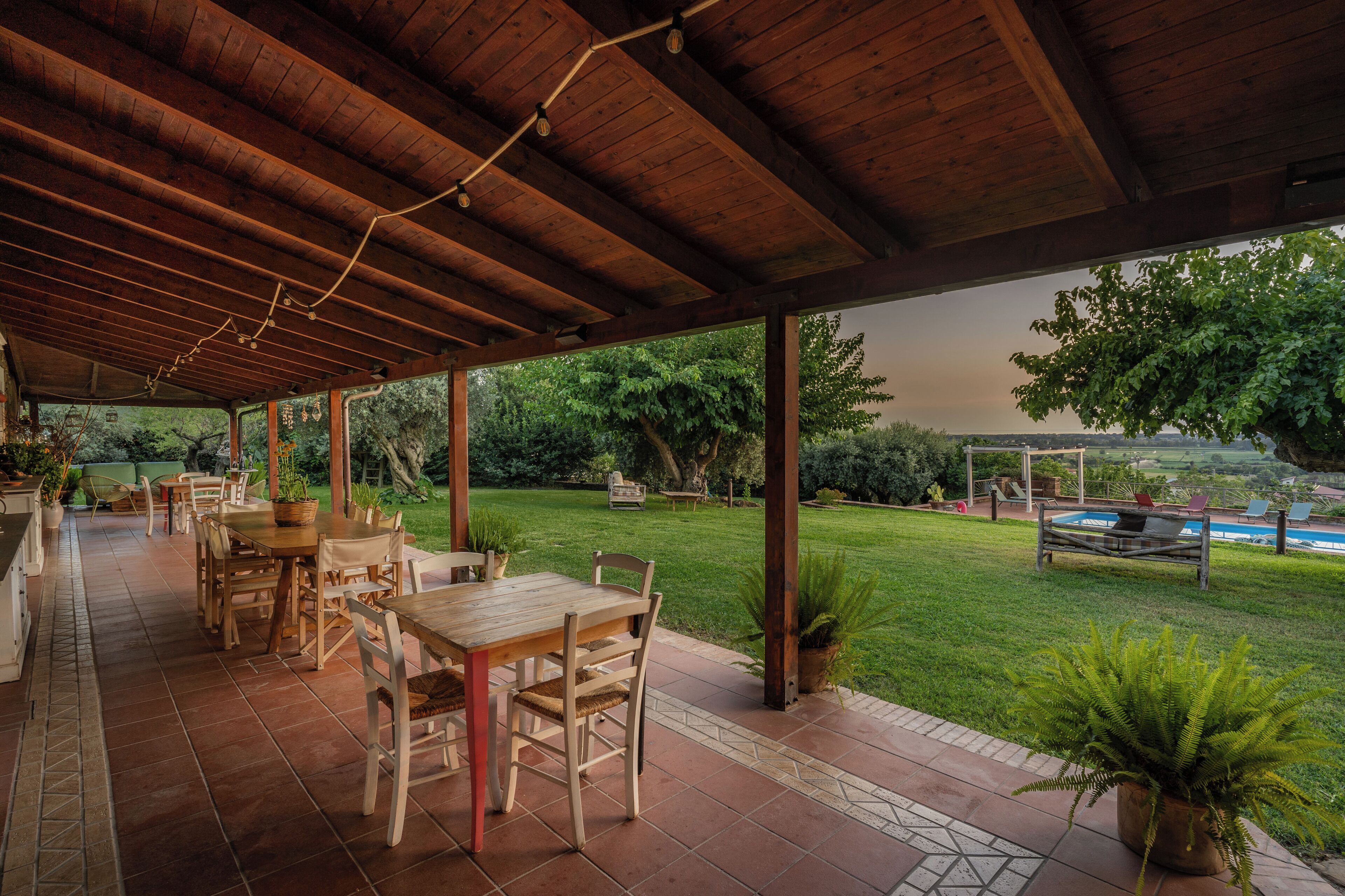 Eine Außenpatio mit Holztischen und -stühlen, einem Pool und Blick auf die umliegende Bepflanzung.