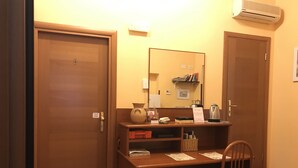 A hotel room with a wooden desk, a chair, a mirror, a bookshelf, and an air conditioning unit. - San Daniele Bundi House (Rome)