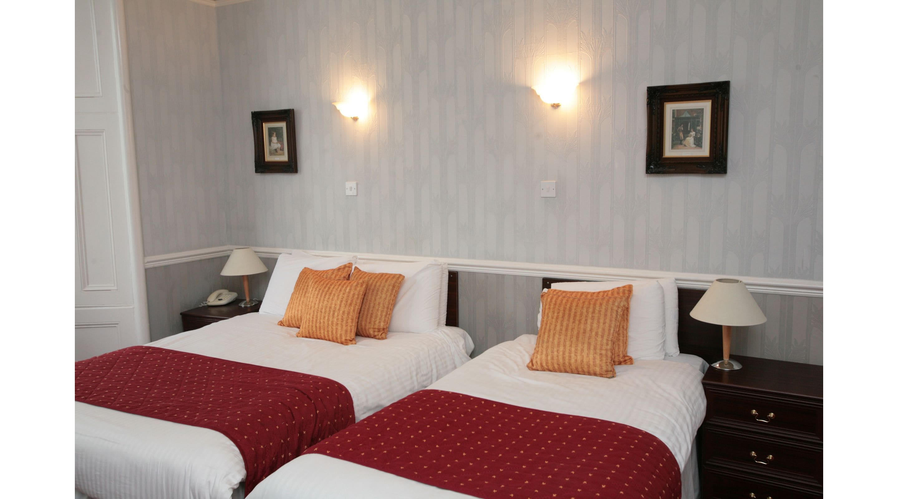 Habitación de hotel con dos camas, cada una con una colcha roja y blanca, y dos lámparas fijadas a la pared.