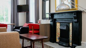 A living room with a fireplace, a television mounted on the wall, and a red chair. - City Apartments Glasgow (Glasgow)