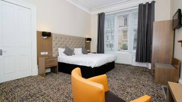 A hotel room with a bed, a chair, a desk, and a window with curtains.