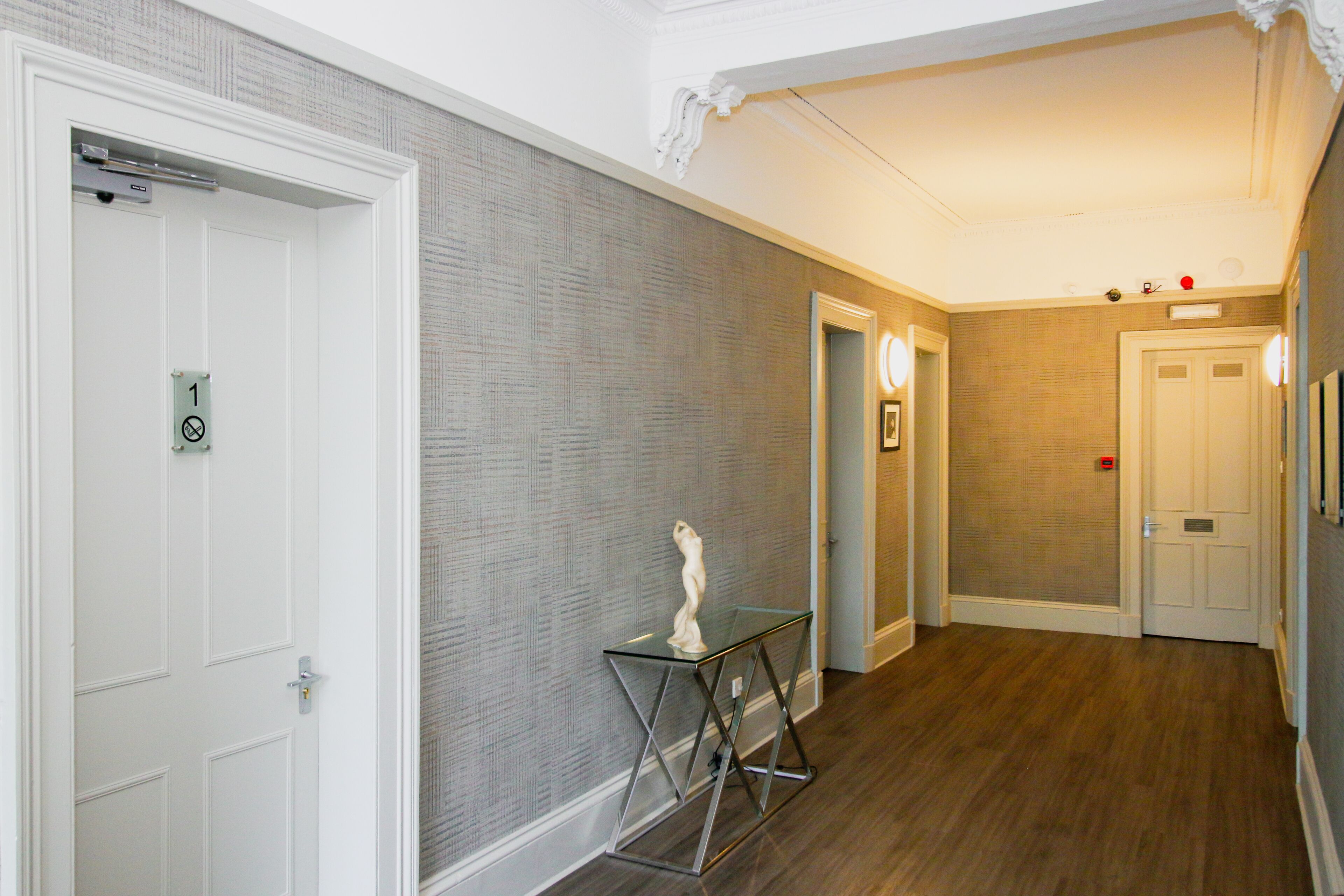 A hallway with a textured wall, a glass table with a sculpture, and a door with a number sign.