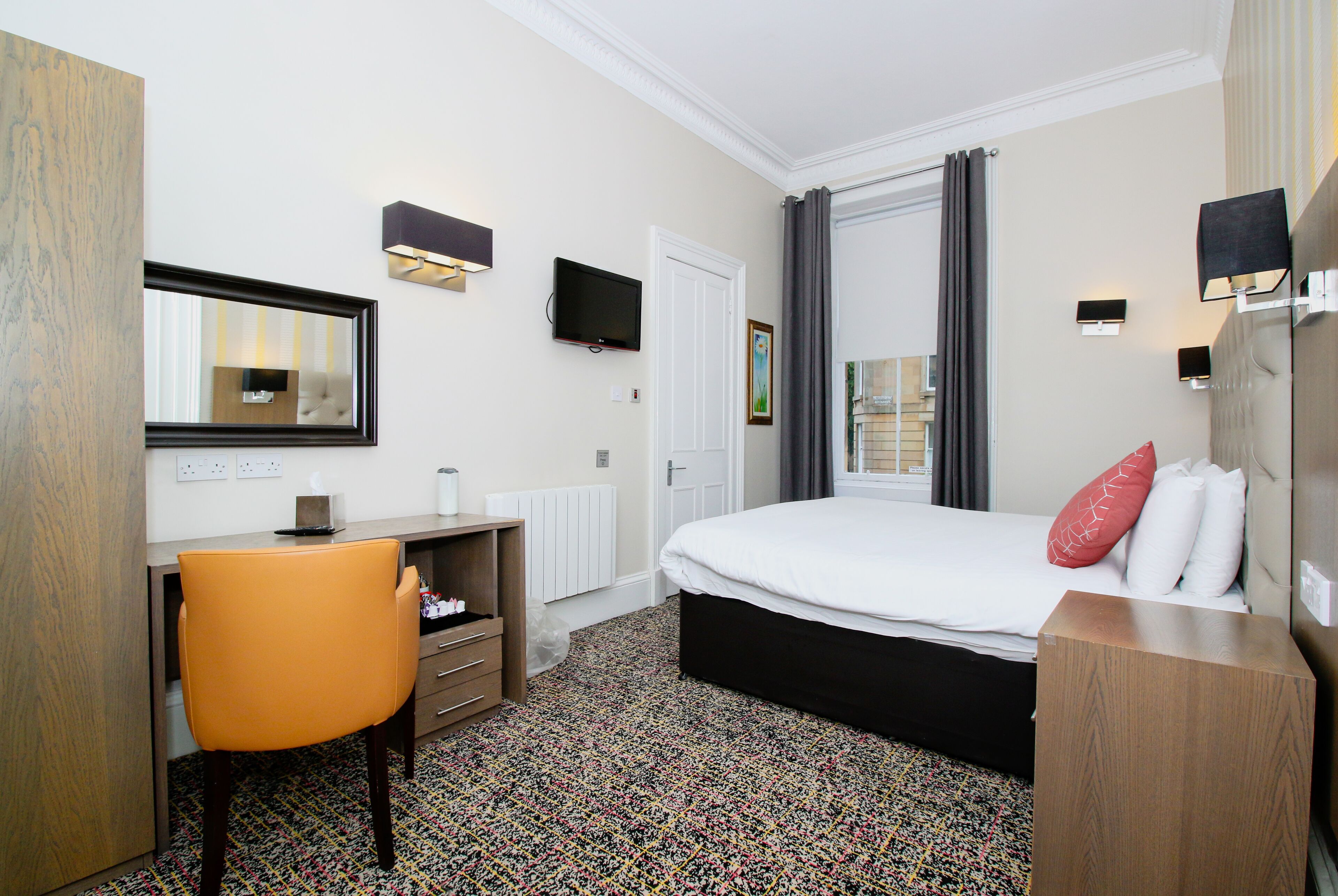 A hotel room with a bed, a desk, a chair, a television, and a window with curtains.