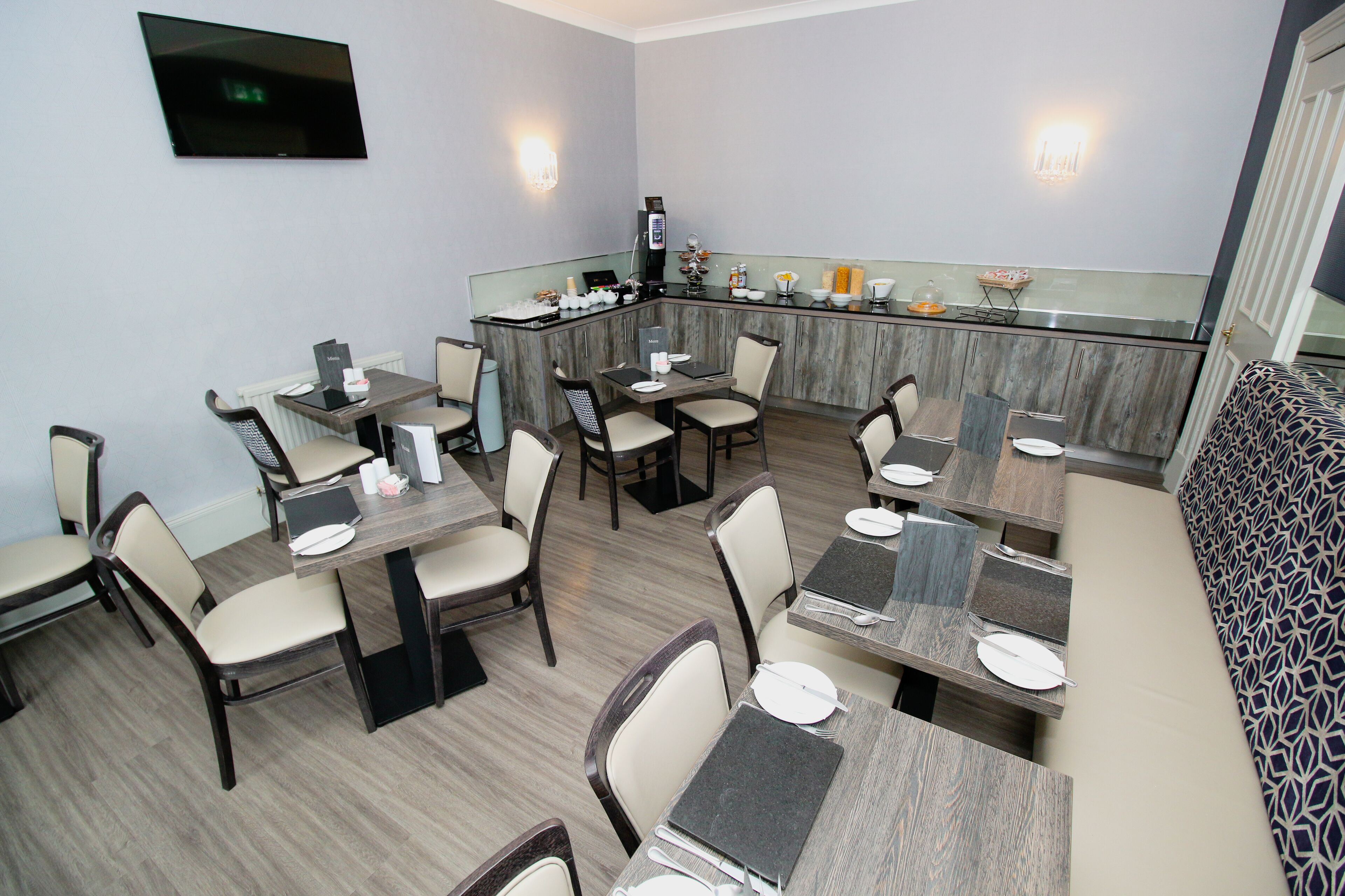 Um restaurante com várias mesas e cadeiras, um balcão com uma máquina de café e uma televisão fixada na parede.