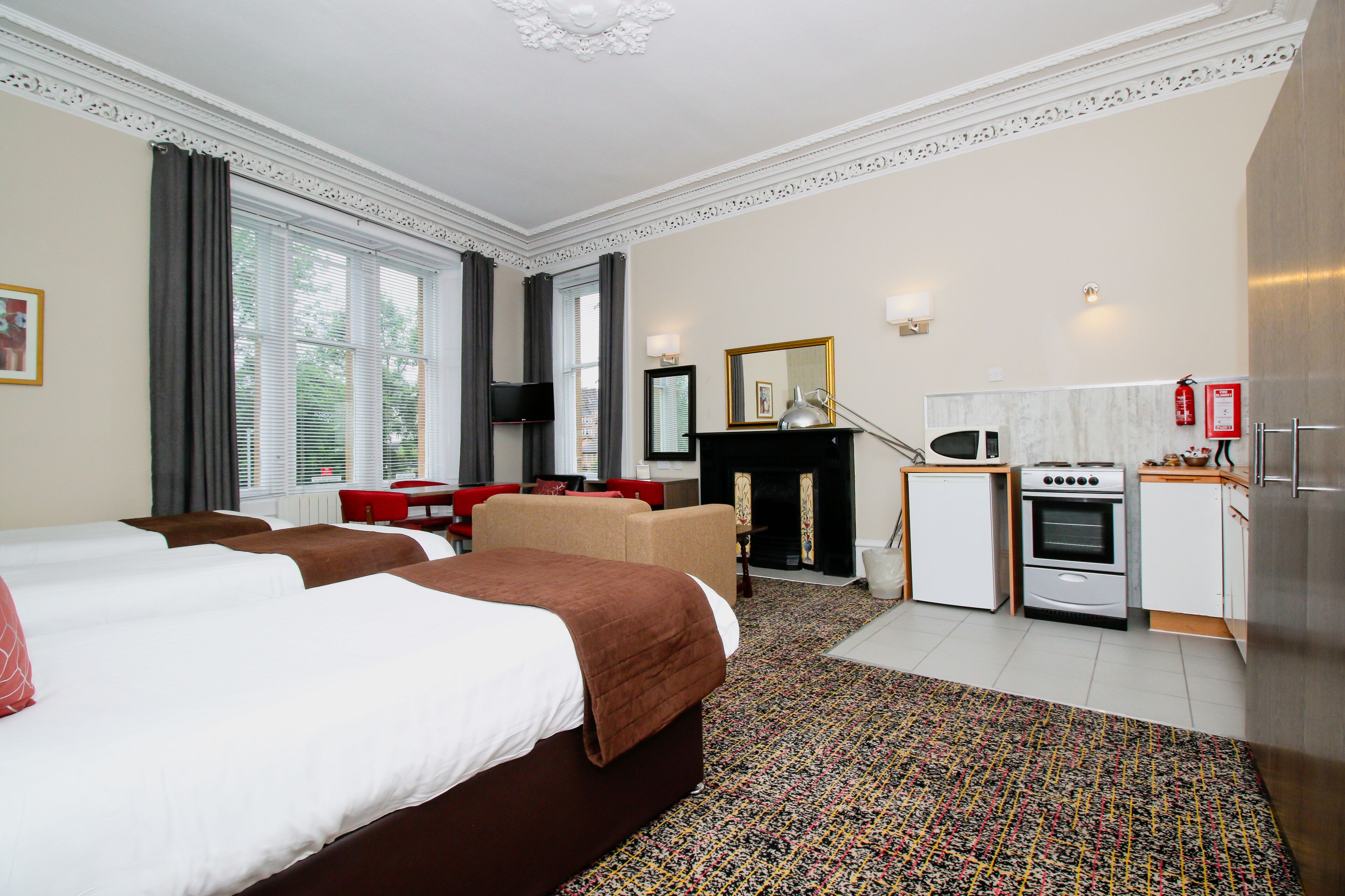 Ein Hotelzimmer mit zwei Betten, einem Esstisch, einer Couch, einem Fernseher, einem Kamin und einer Küchenzeile.