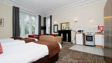 Ein Hotelzimmer mit zwei Betten, einem Esstisch, einer Couch, einem Fernseher, einem Kamin und einer Küchenzeile.