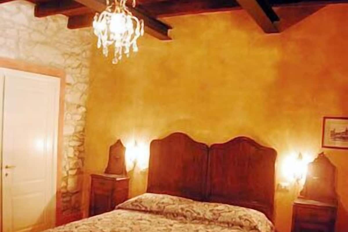 A bedroom with a wooden bed, stone wall, and a chandelier.