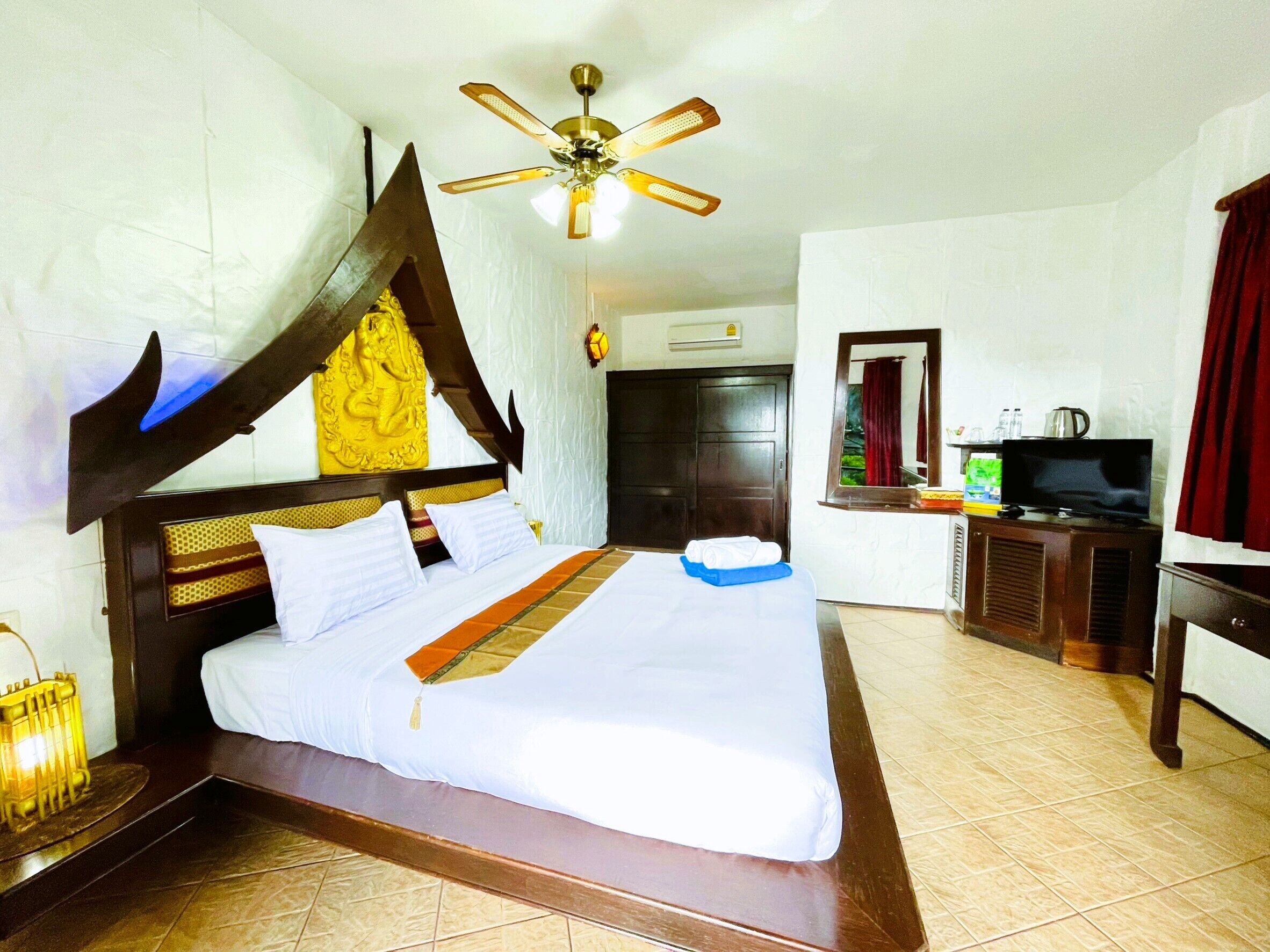 A hotel room with a large bed, a ceiling fan, a television, and a minibar.