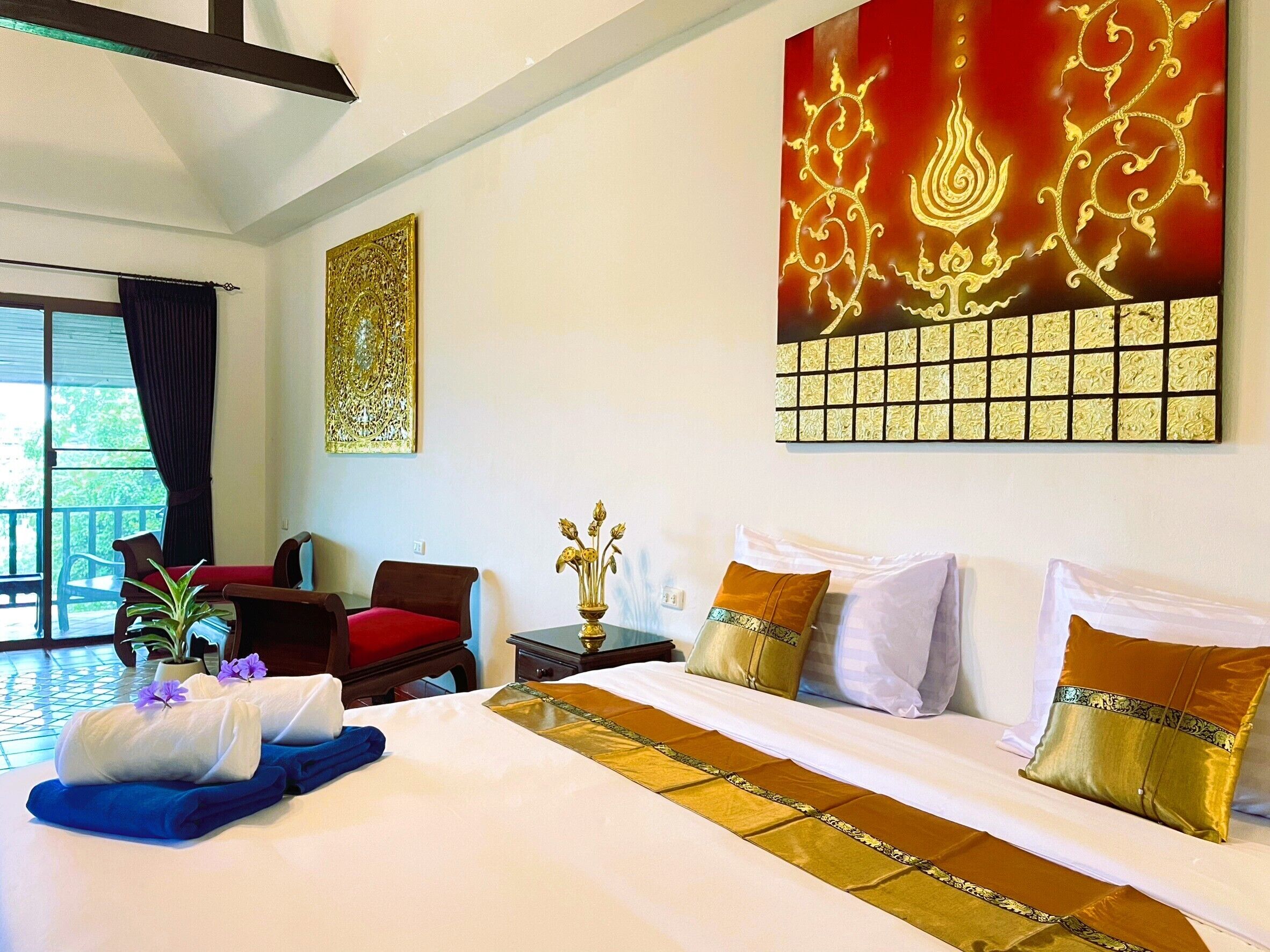 A hotel room with a large bed, a red chair, a small table with a vase, and a large decorative wall piece.