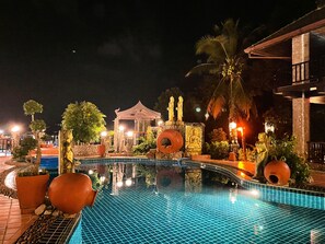 A nighttime pool area with a tiled surface, surrounded by statues and a gazebo. - Boomerang Village Resort Kata (Karon)