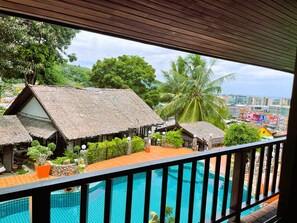 A pool area with a view of thatched-roof buildings and palm trees. - Boomerang Village Resort Kata (Karon)