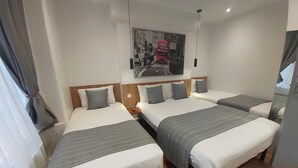 A hotel room with three single beds, a wooden headboard, a cityscape painting, and a wooden floor. - Falcon Hotel (London)