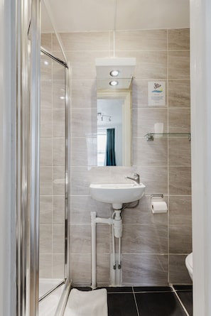 A modern bathroom with a glass shower enclosure, a white sink, and a mirror above it. - Falcon Hotel (London)