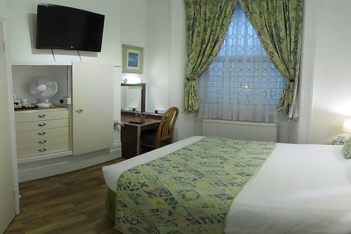 A hotel room with a bed, bedside table, lamp, and a window with curtains.
