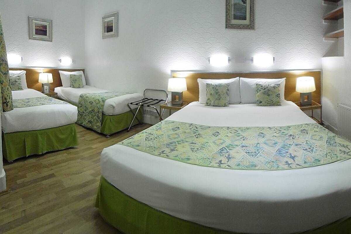 A hotel room with two single beds, a large bed, and a nightstand with a lamp.
