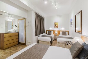 A hotel room with two beds, a wooden dresser, a desk with a hairdryer, and a mirror. - Falcon Hotel (London)