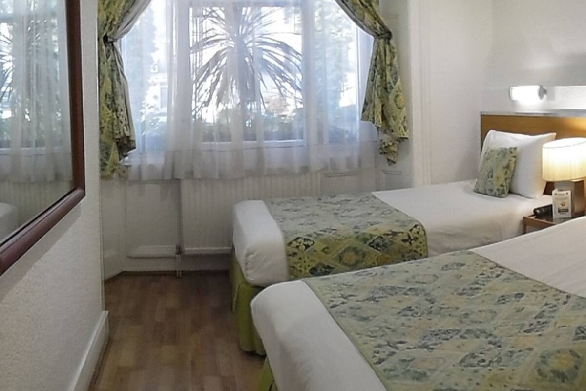A hotel room with two beds, a desk, a chair, a lamp, and a window with curtains.