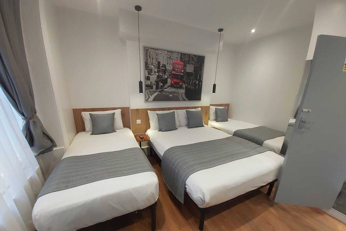 A hotel room with two single beds, a wooden headboard, a nightstand, and a grey door.