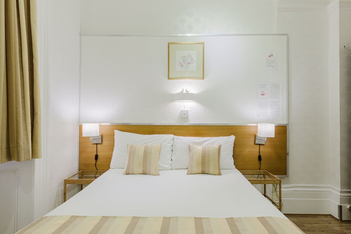 A hotel room with a large bed, two bedside lamps, a wooden headboard, and a framed picture on the wall.
