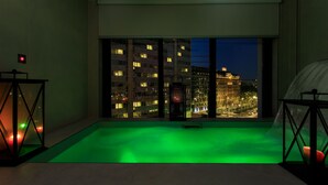 Un balcón con suelo iluminado en verde, ventanas amplias y vista nocturna de la ciudad.