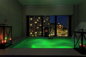 A room with a view of a cityscape at night, a green-lit pool, and a red-lit table lamp. - iQ Hotel Milano (Milan)