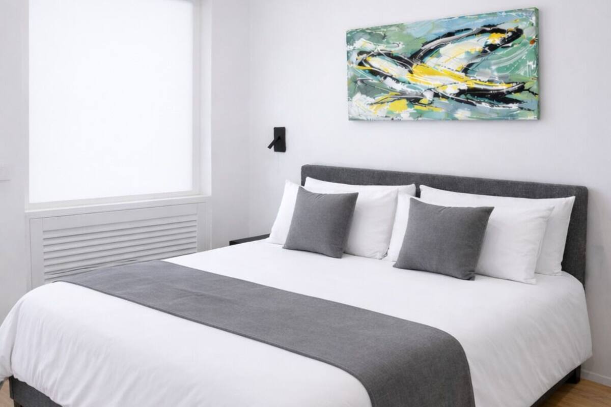 A modern bedroom with a bed, white walls, a window, and a painting.