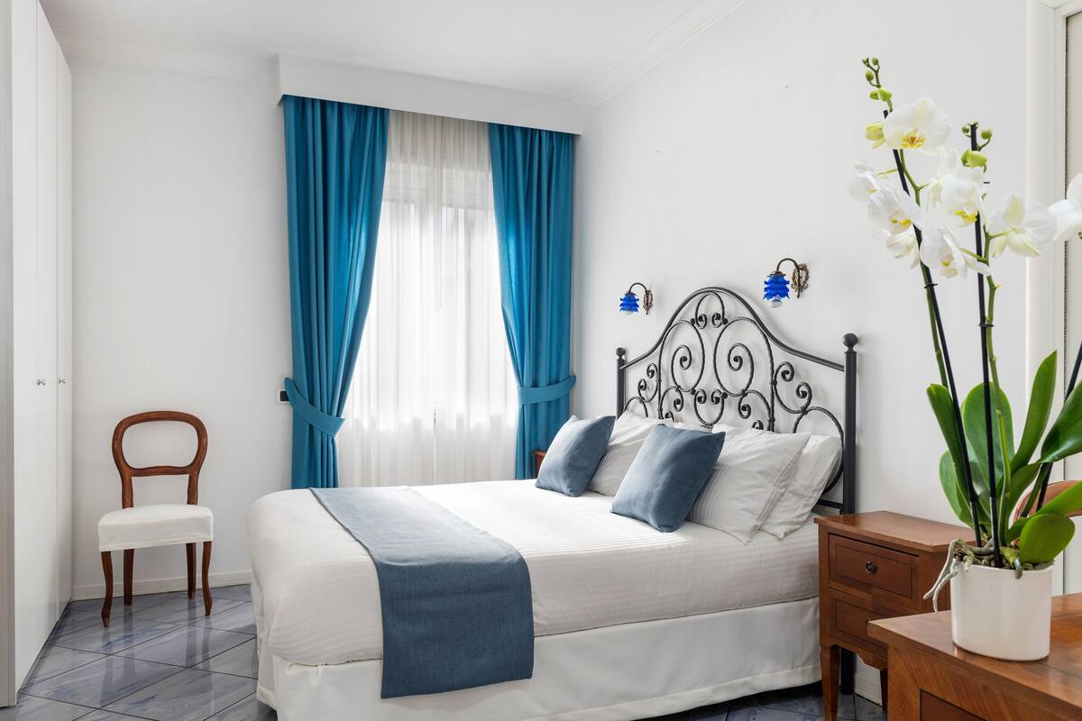 A neatly arranged bedroom with a bed, a chair, a nightstand, and a potted plant.