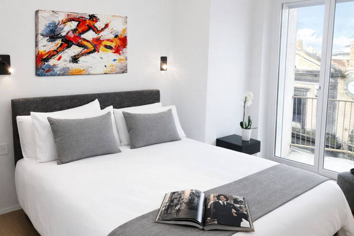 A modern bedroom with a large bed, a city view, and a painting on the wall.