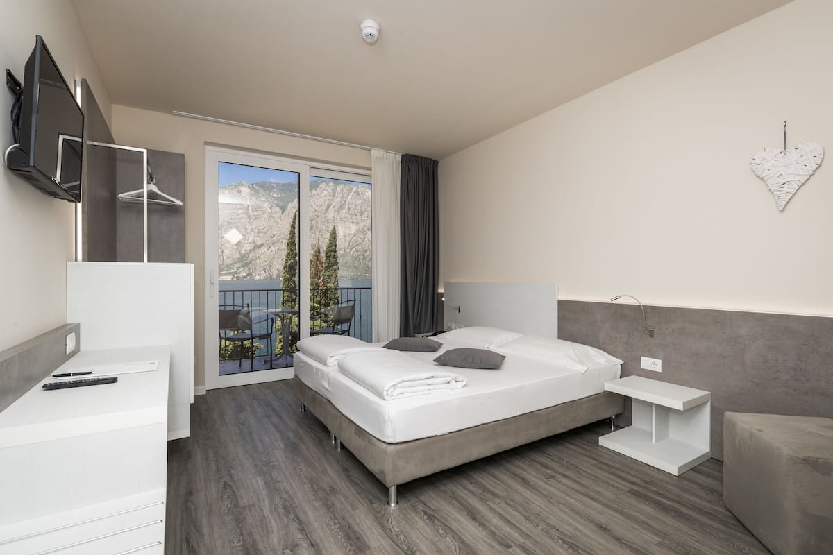 A modern hotel room with a large bed, a desk, a chair, and a balcony with a mountain view.