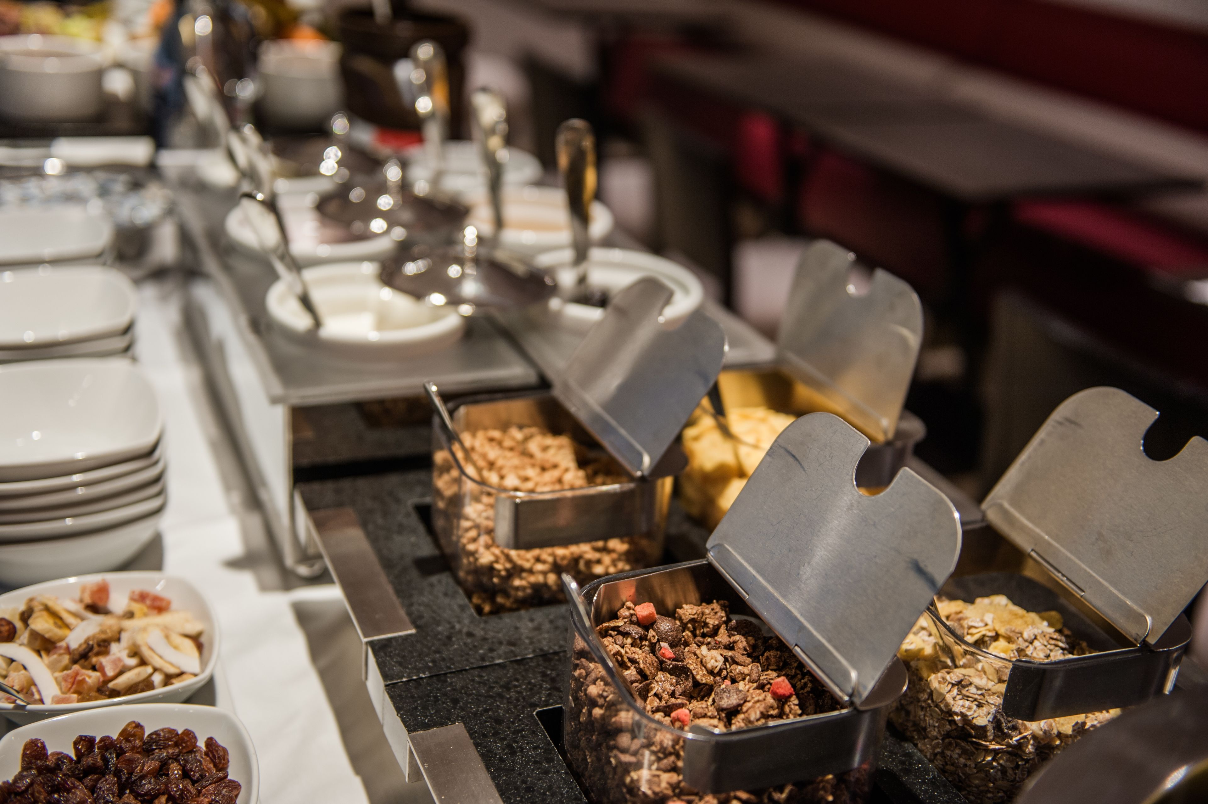 A buffet setup with various food items in metal containers, including cereals and fruits.