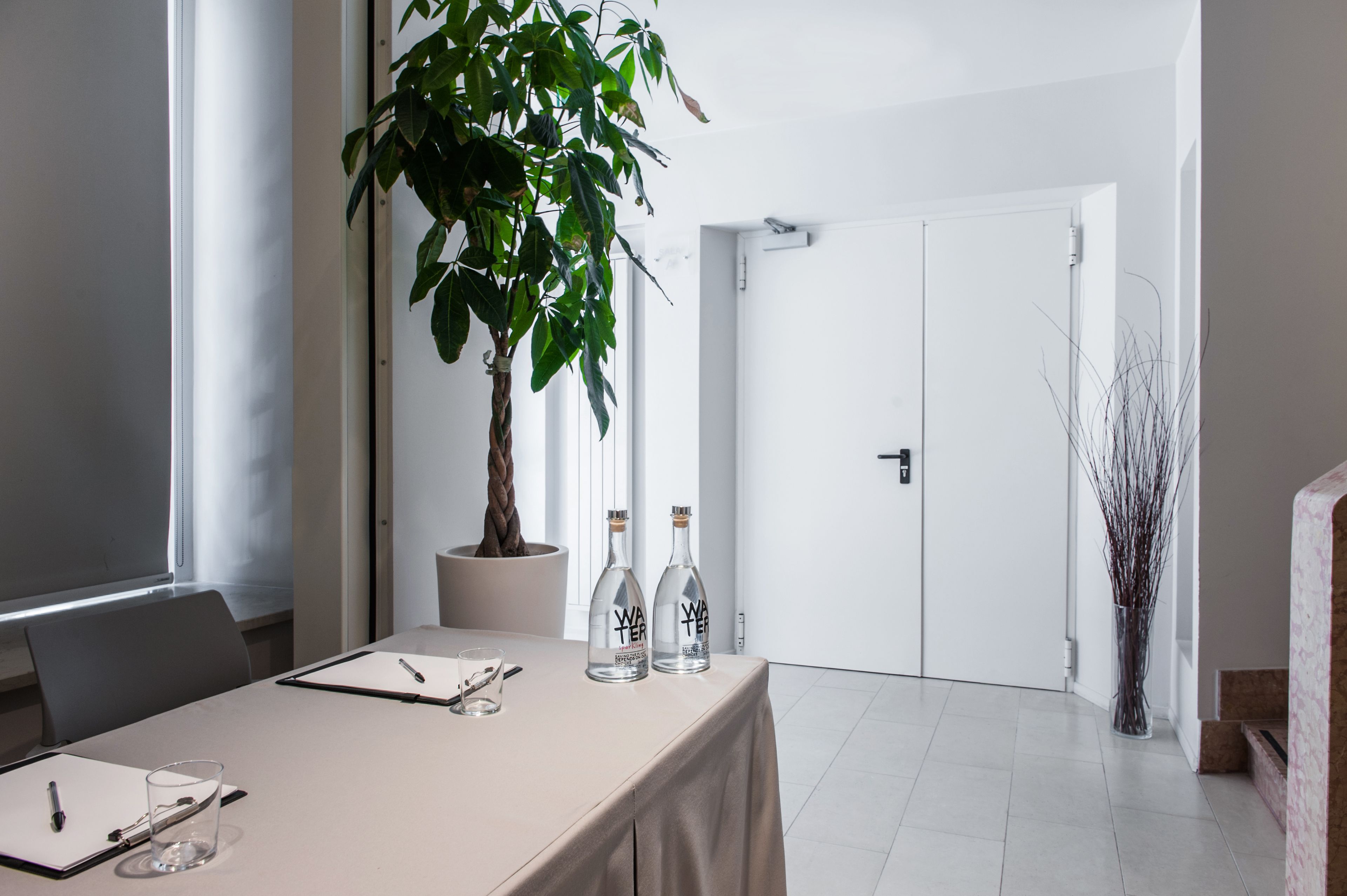 Ein Konferenzraum mit Tisch, zwei Wasserflaschen, einer Topfpflanze und einer Whiteboard-Wand.