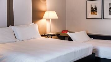 A hotel room with two beds, a bedside table with a lamp, and two framed pictures on the wall.