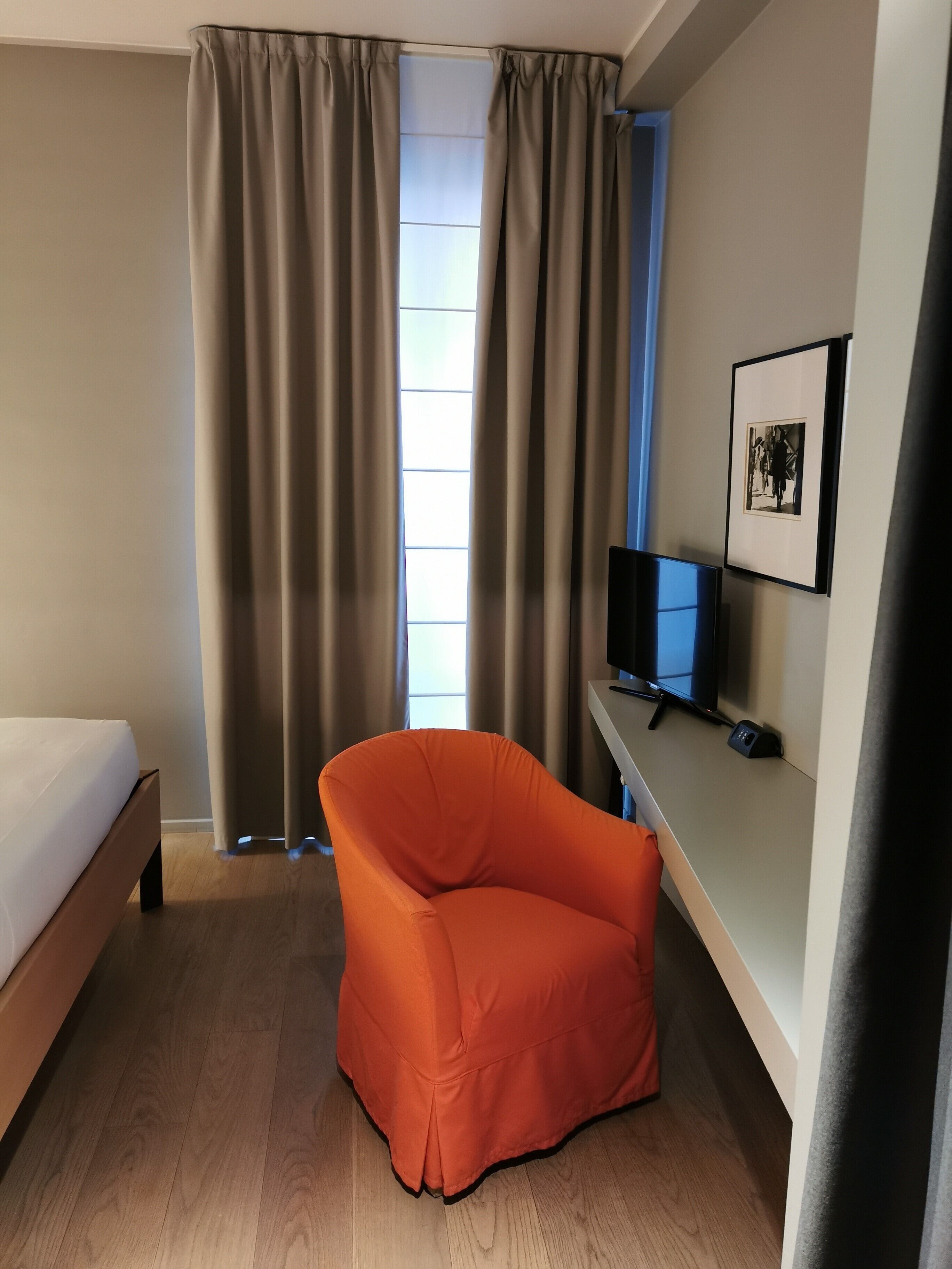 Habitación de hotel con cama, escritorio con computadora, silla y ventana con cortinas.