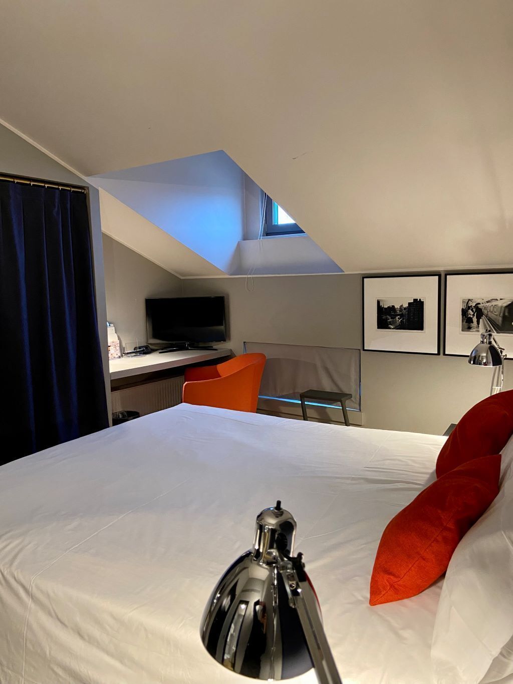 A hotel room with a bed, a desk, a chair, a TV, and a skylight.