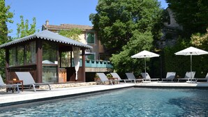 A swimming pool with lounge chairs and umbrellas, a gazebo, and a building with a balcony overlooking the pool.