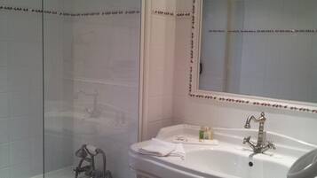 A bathroom with a glass-enclosed shower, a pedestal sink, and a mirror with a decorative border.