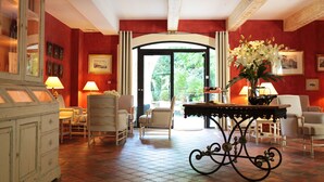 A spacious room with a tiled floor, a large window, and a door leading outside. There are several chairs and a table with a vase of flowers.