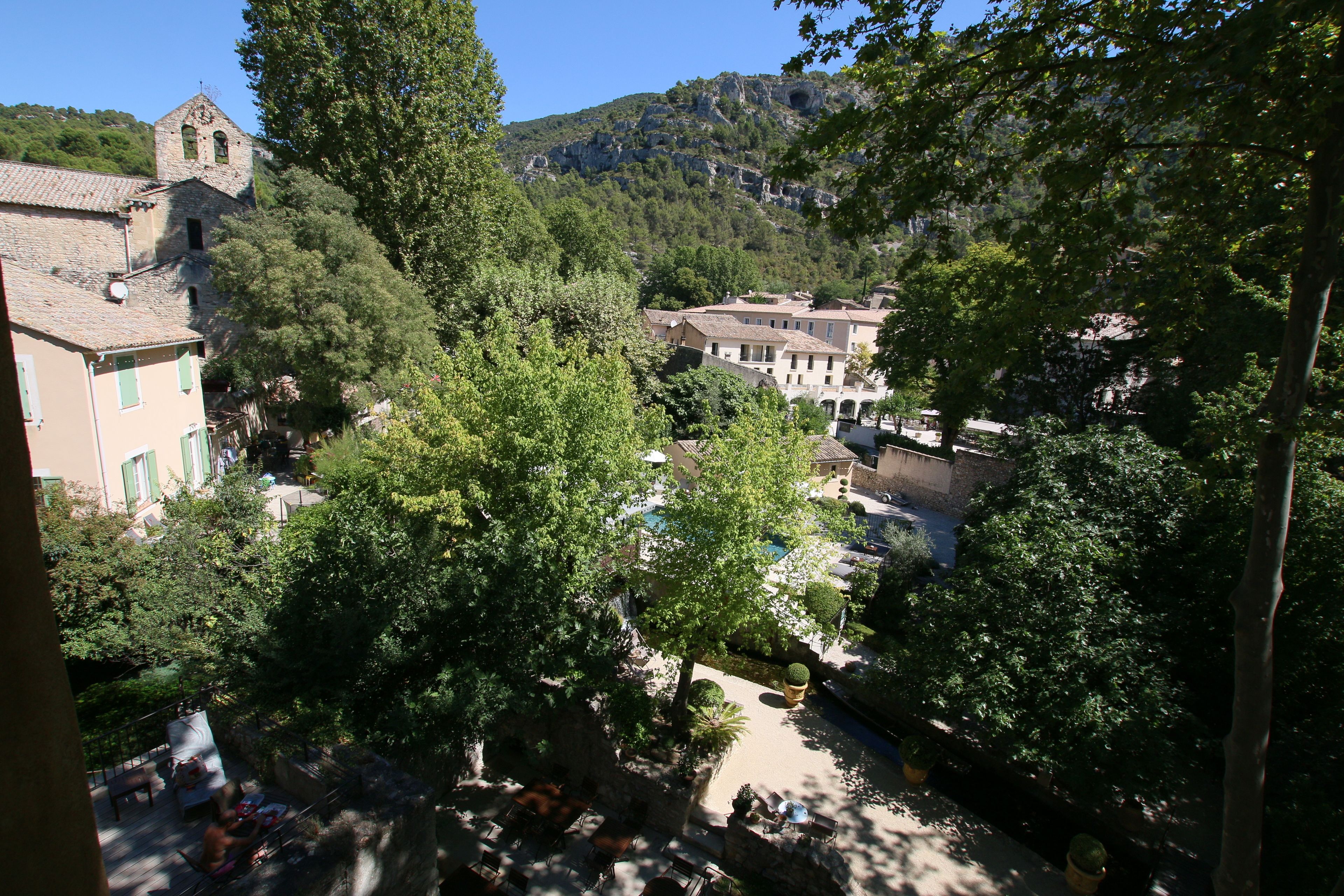 A courtyard with outdoor seating, surrounded by trees and buildings, including a church with a bell tower.