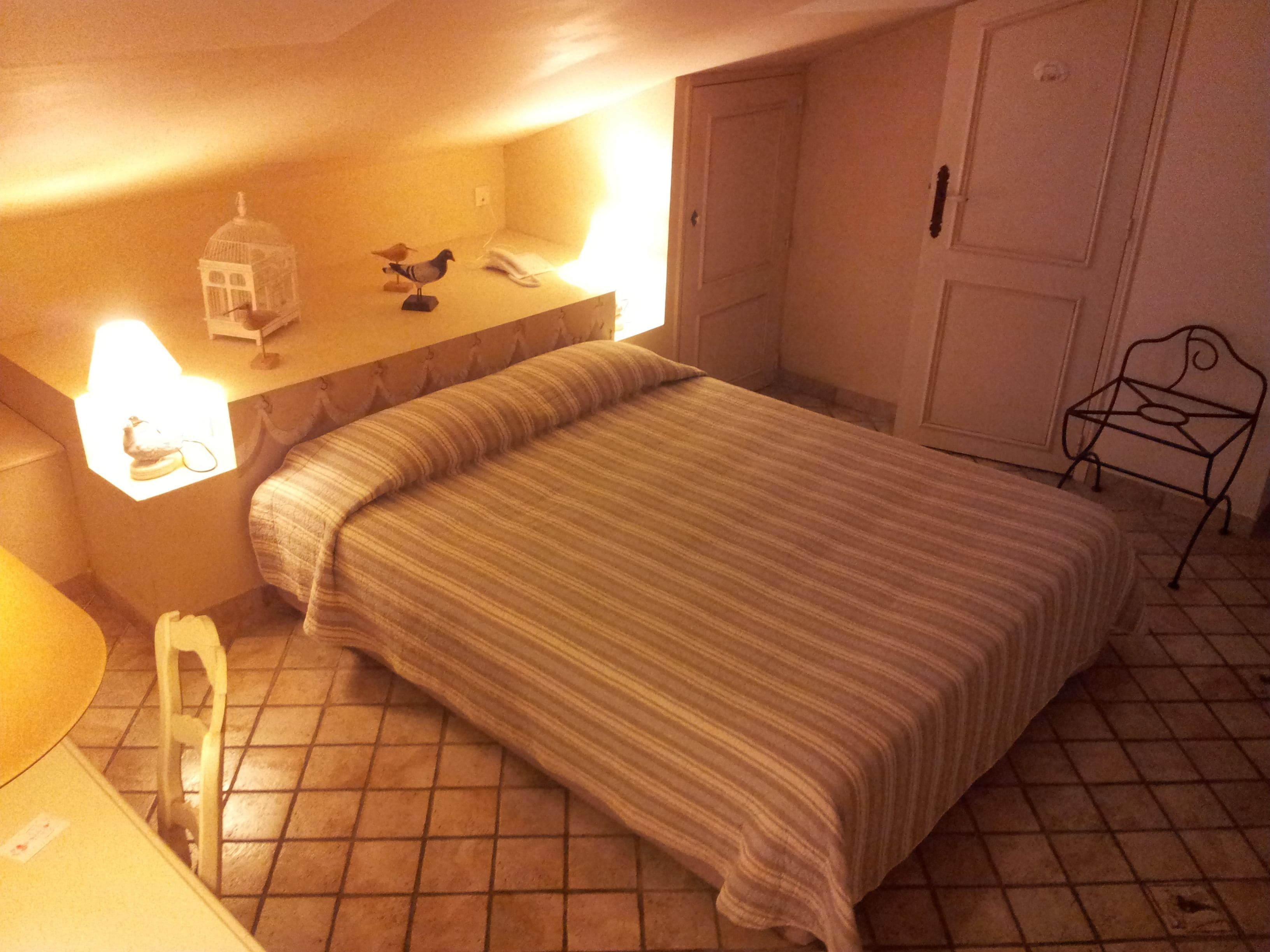 A bedroom with a bed, a nightstand, a lamp, a pigeon sculpture, and a door.