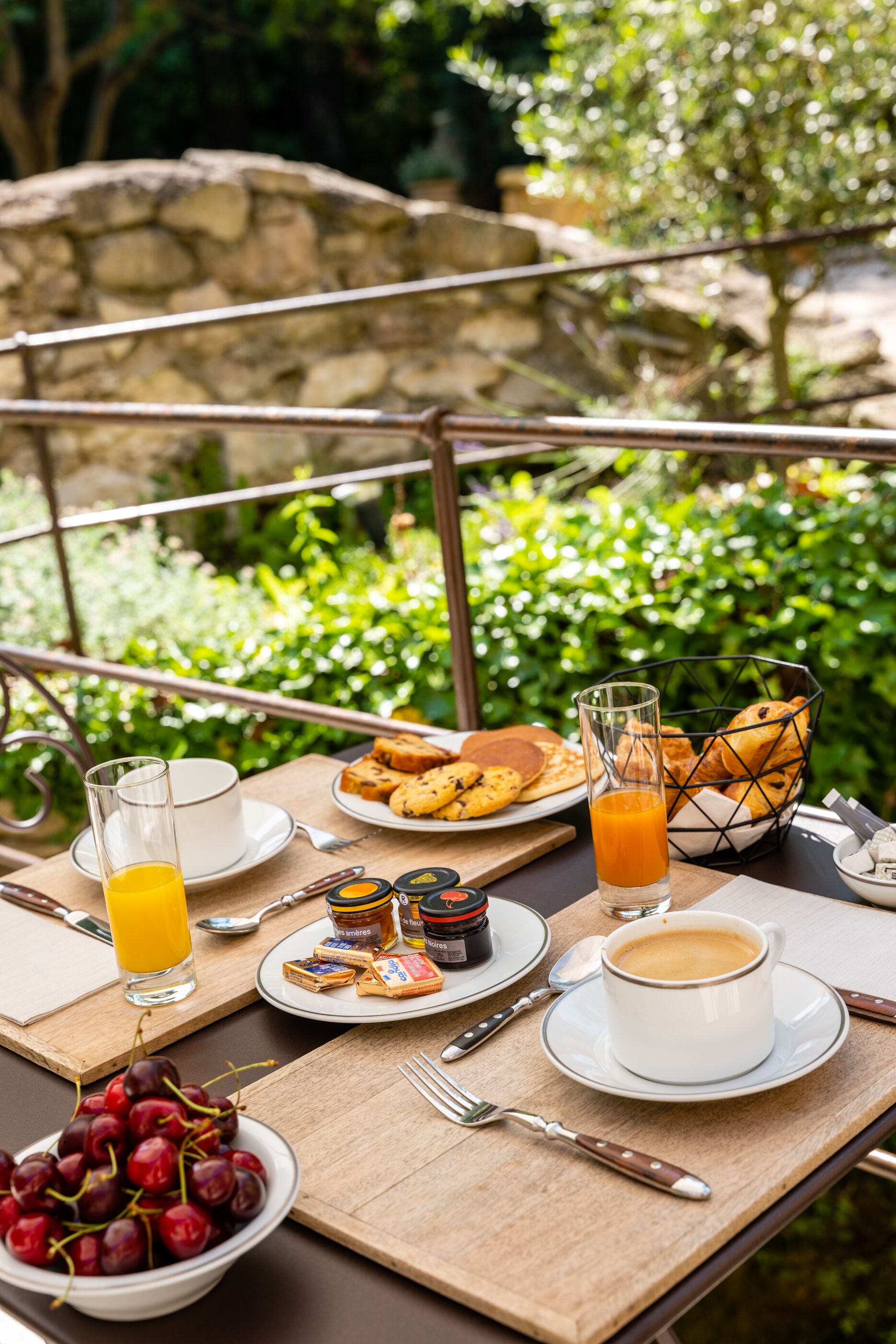 A breakfast table set outdoors with a stone wall and greenery in the background.