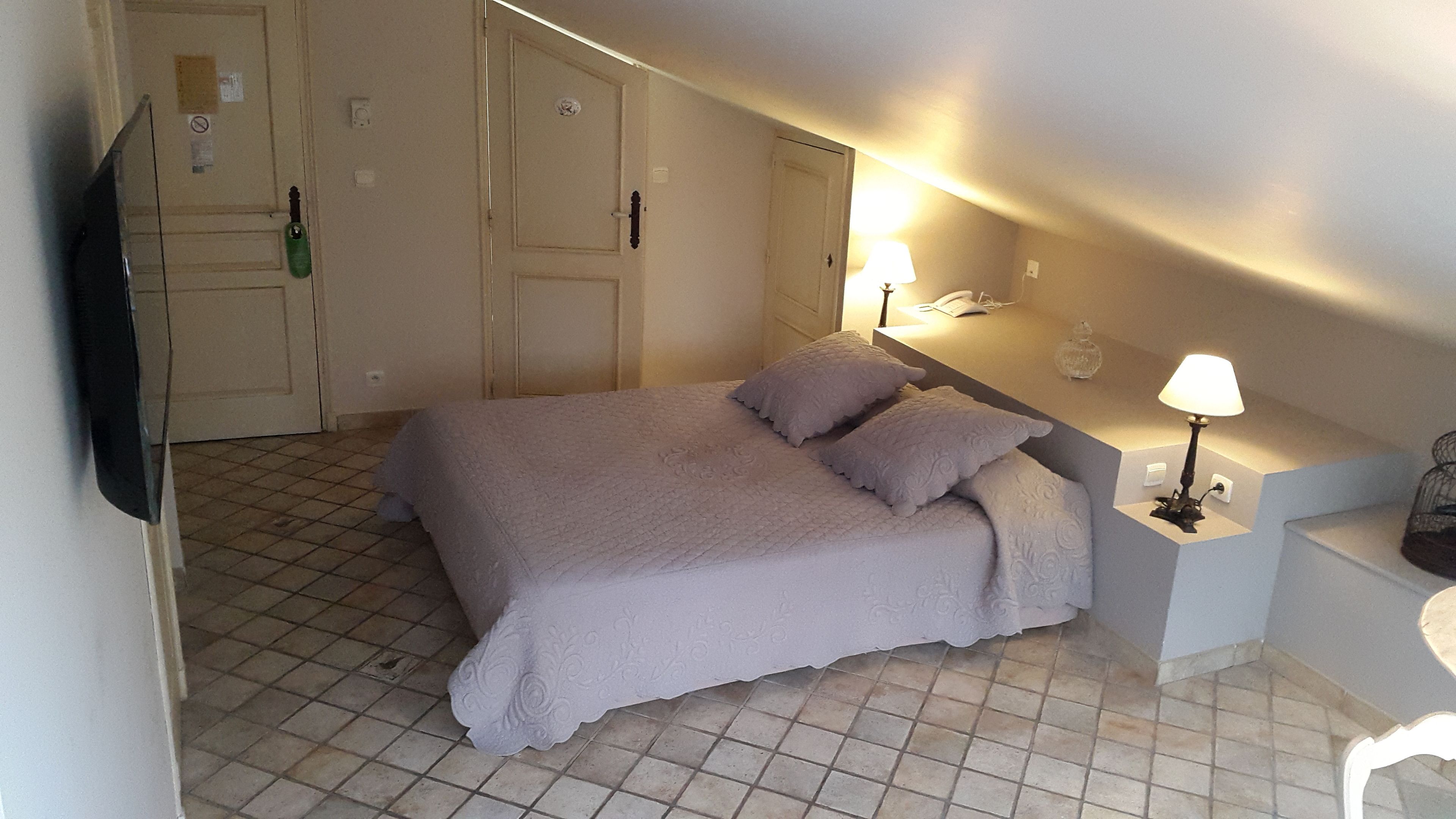 Ein Schlafzimmer mit einem Bett, zwei Nachttischlampen, einem Nachttisch und einem Fliesenboden.