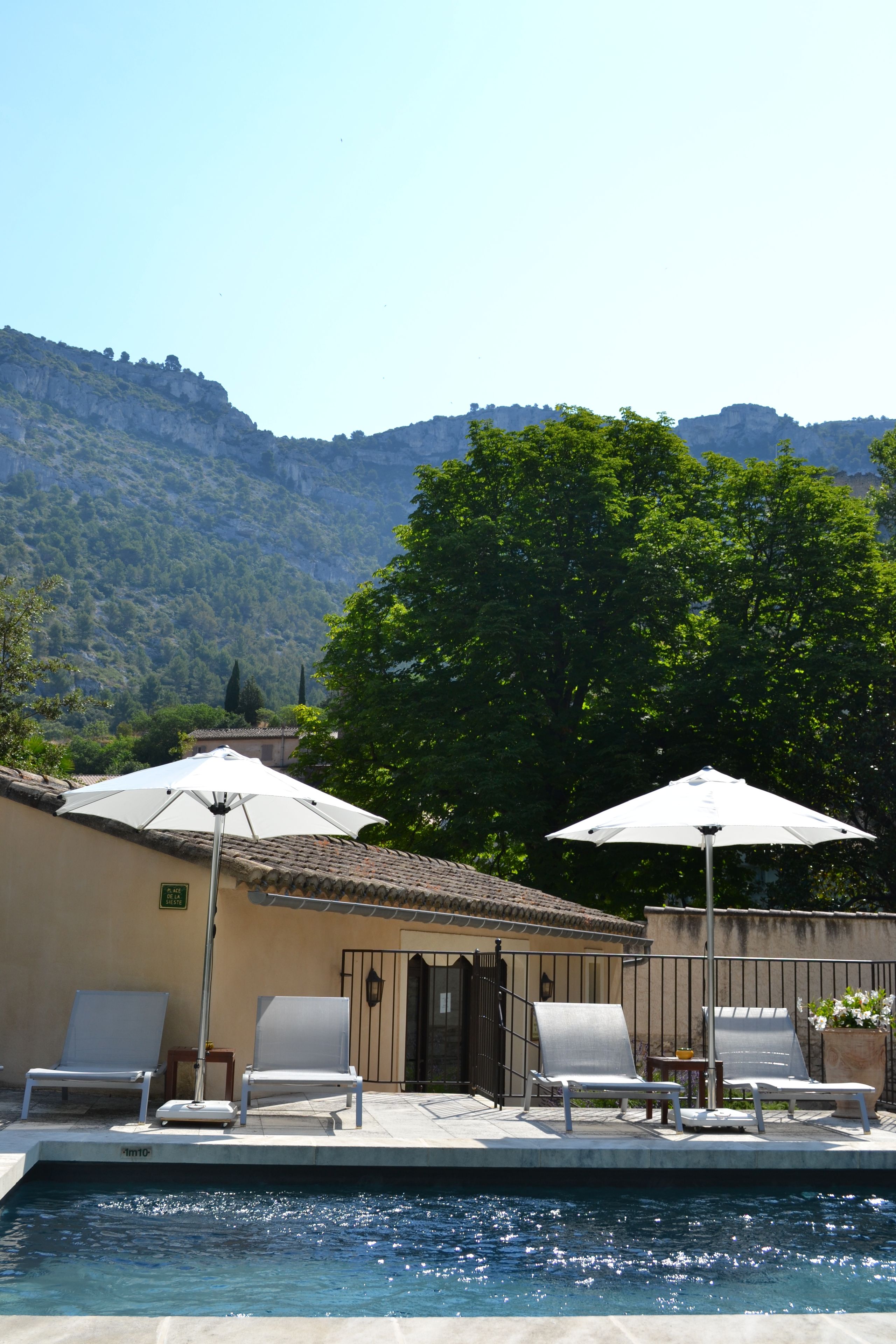 Ein Poolbereich mit Liegestühlen und Sonnenschirmen, ein Ziegeldach und ein Berg im Hintergrund.