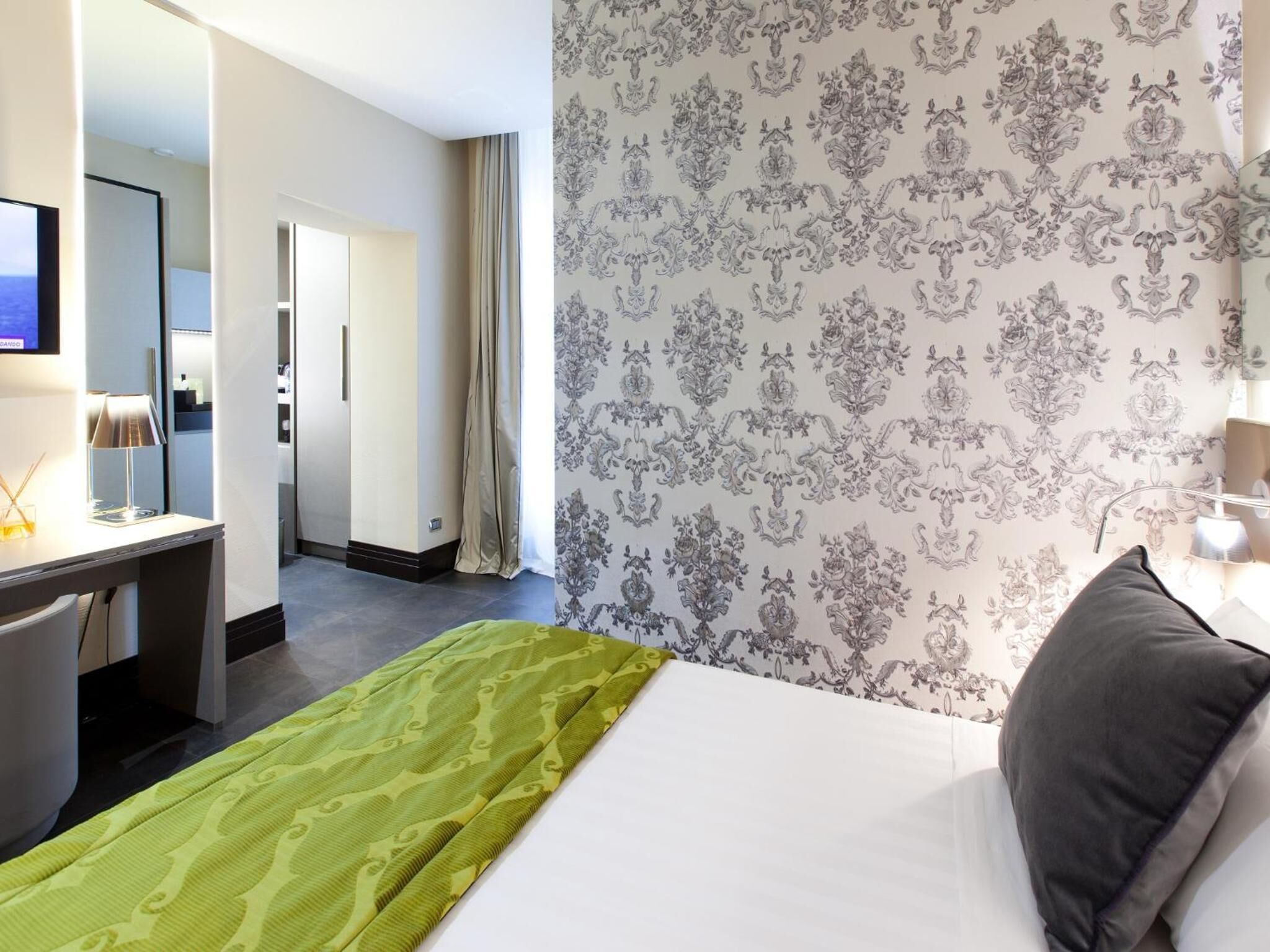 Ein Hotelzimmer mit Bett, Schreibtisch, Spiegel und einem durch eine offene Tür einsehbaren Badezimmer.