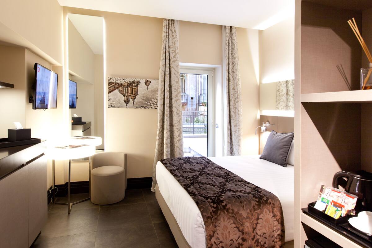 Une chambre d’hôtel comprenant un lit, un bureau avec une chaise, une télévision et une fenêtre avec des rideaux.