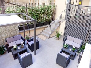 An outdoor patio area with two seating arrangements, a covered section, and a staircase leading to an upper level. - Quirinale Luxury Rooms (Rome)